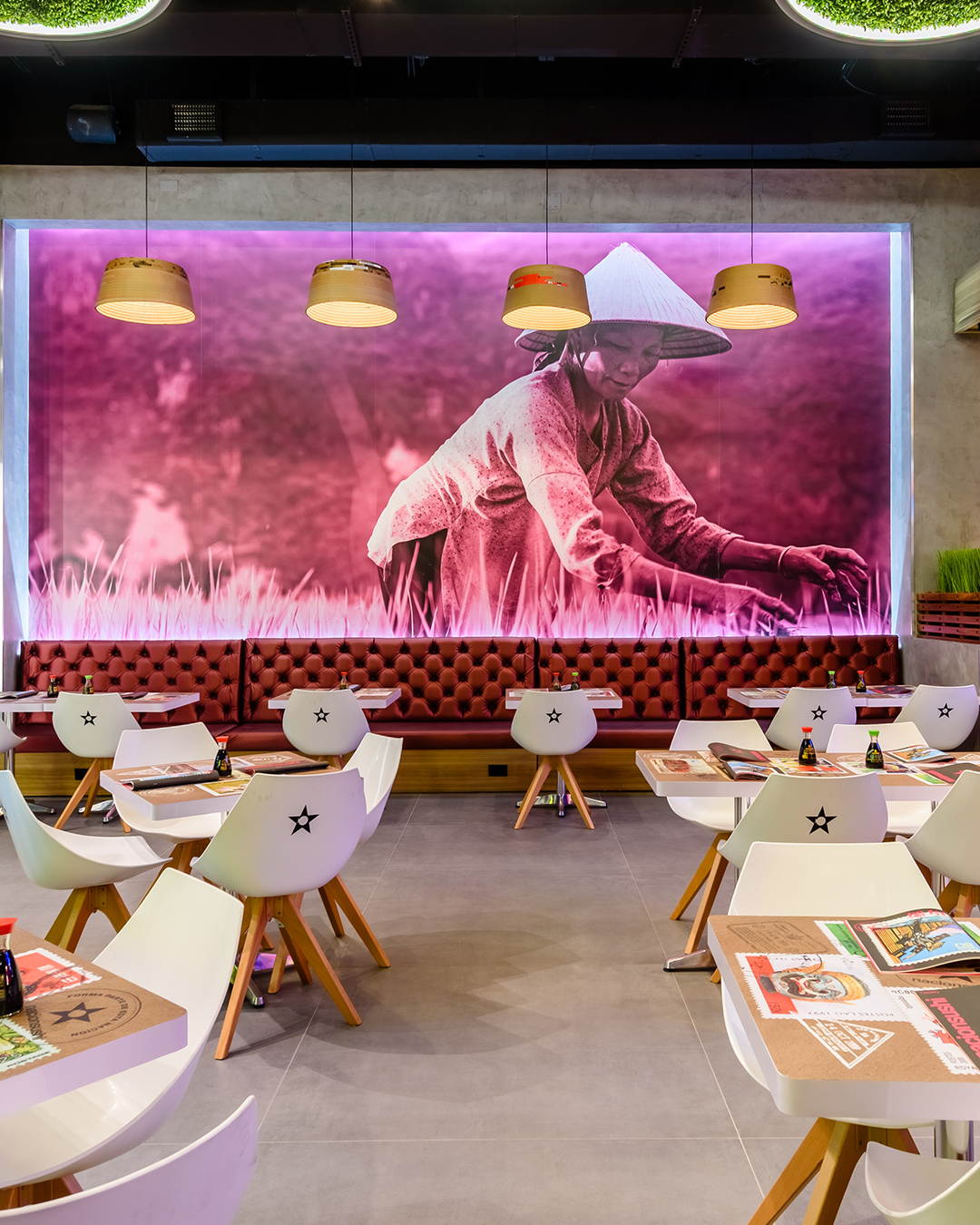 Área de mesas en Nacionsushi con mural decorativo de mujer trabajando en el campo, iluminación cálida y ambiente moderno.