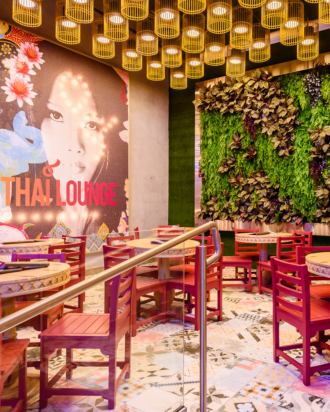Área Thai Lounge en Nacionsushi con mesas redondas, sillas coloridas, lámparas colgantes y mural decorativo.