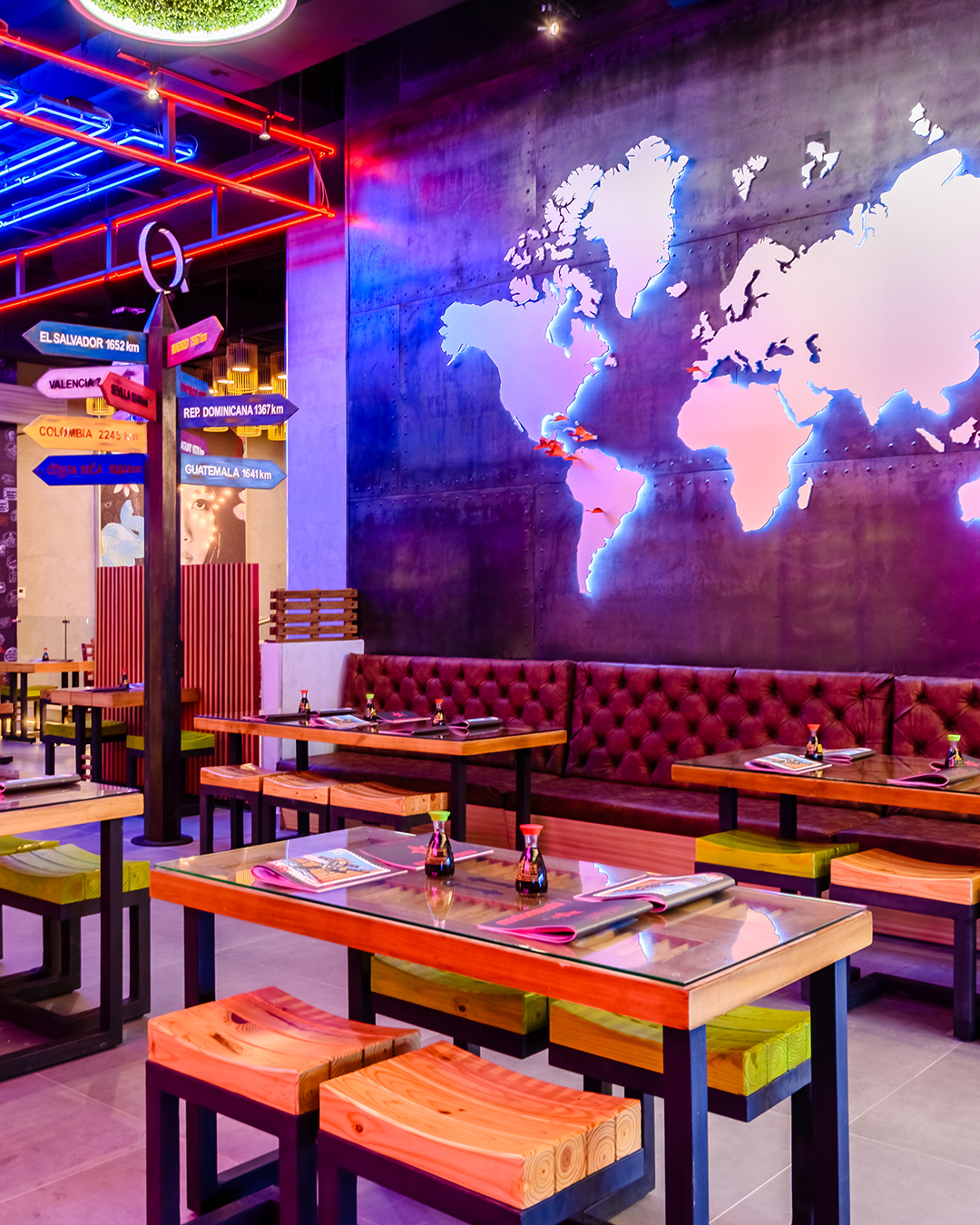 Área de mesas en Nacionsushi con mural de mapa mundial iluminado, mesas de madera y ambiente moderno con luces de neón.