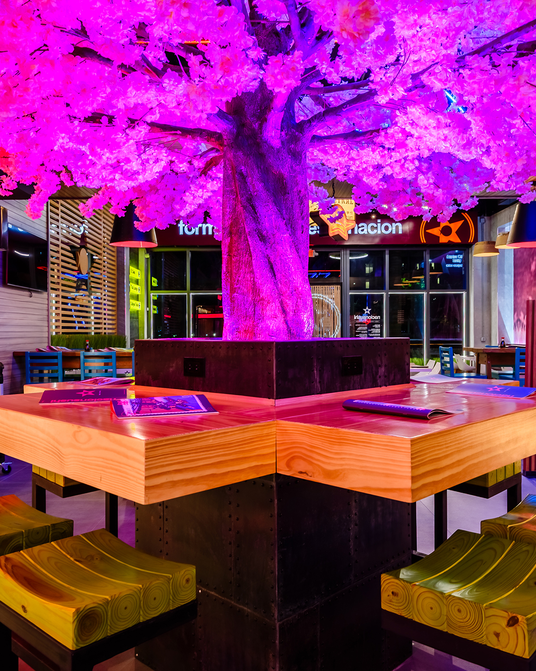 Mesa central de Nacionsushi con árbol decorativo iluminado en tonos rosados y menús sobre la superficie de madera.