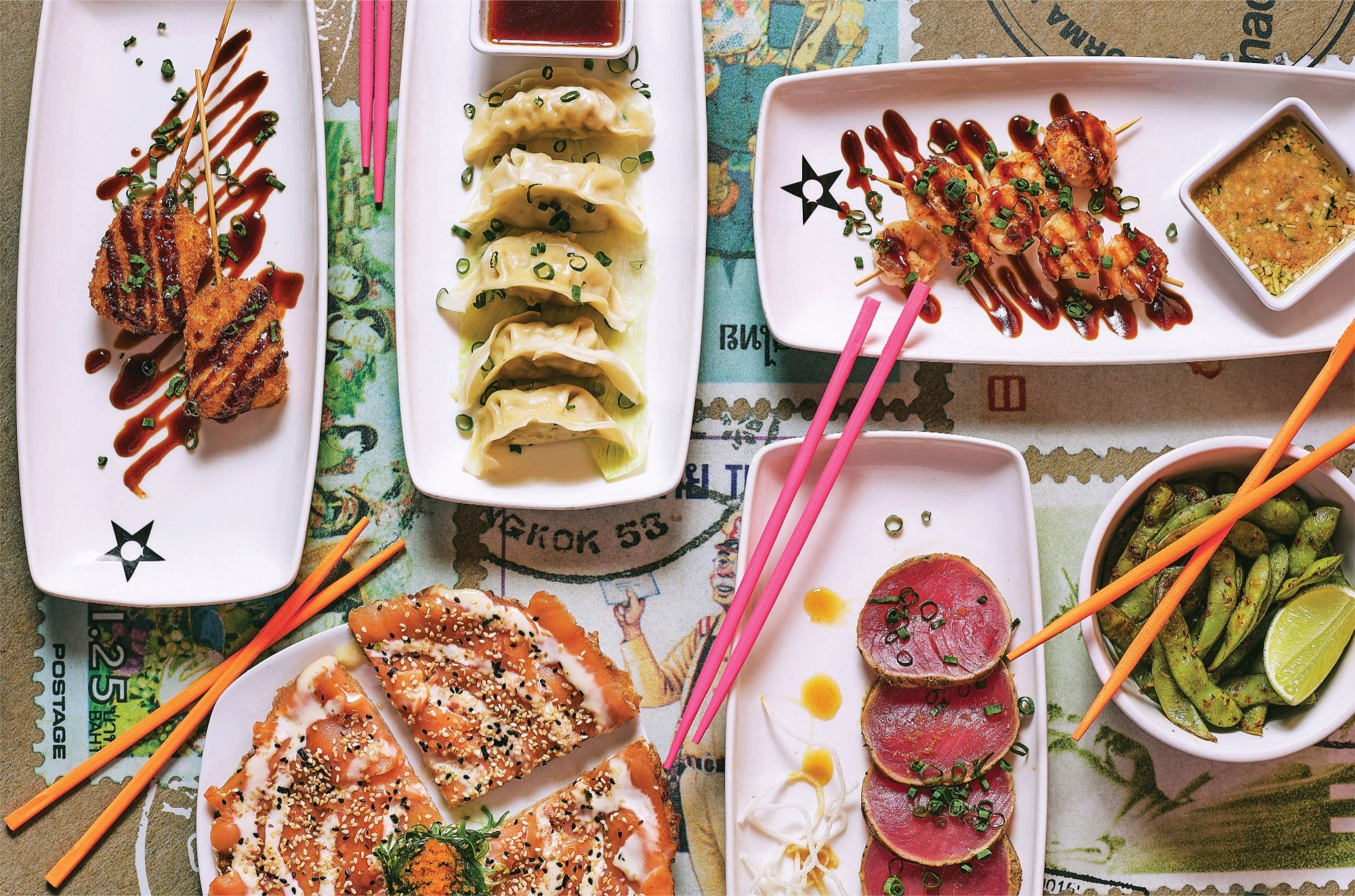 Selección de entradas asiáticas de Nacionsushi con gyozas, brochetas, edamame y platos variados servidos en vajilla blanca.